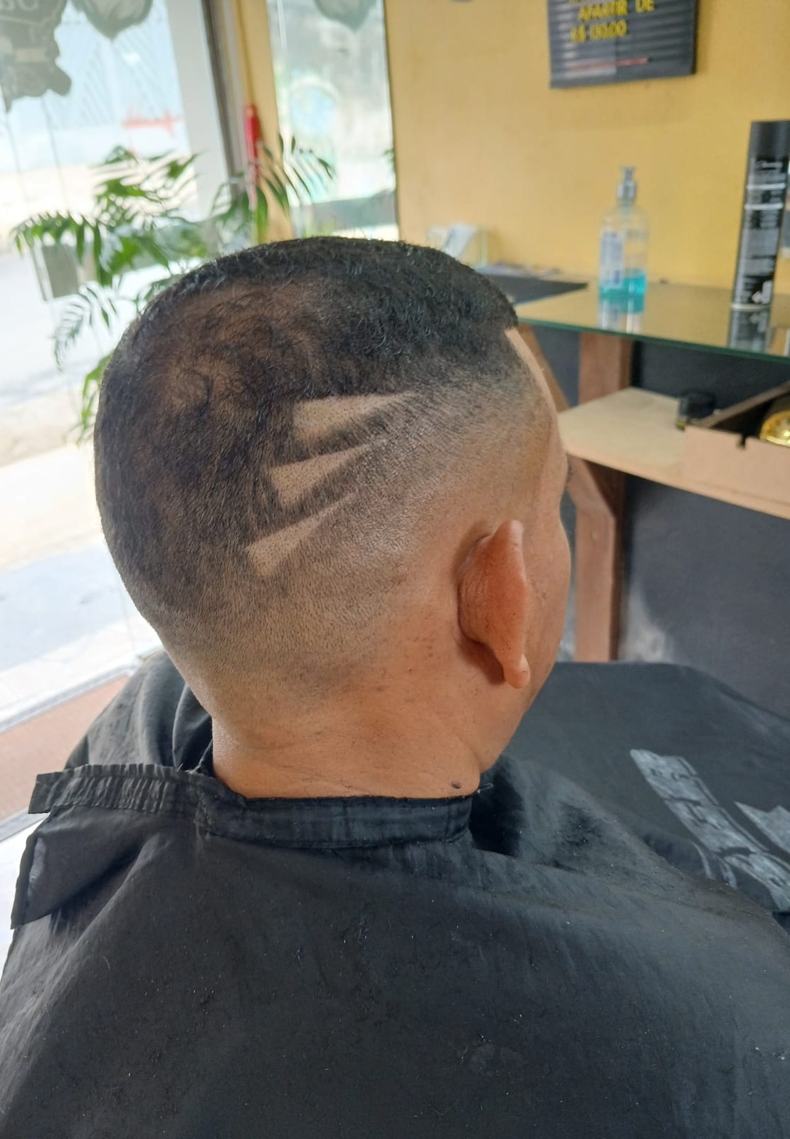 traseira de corte degradê com desenho raspado na nuca, cliente com capa de atendimento